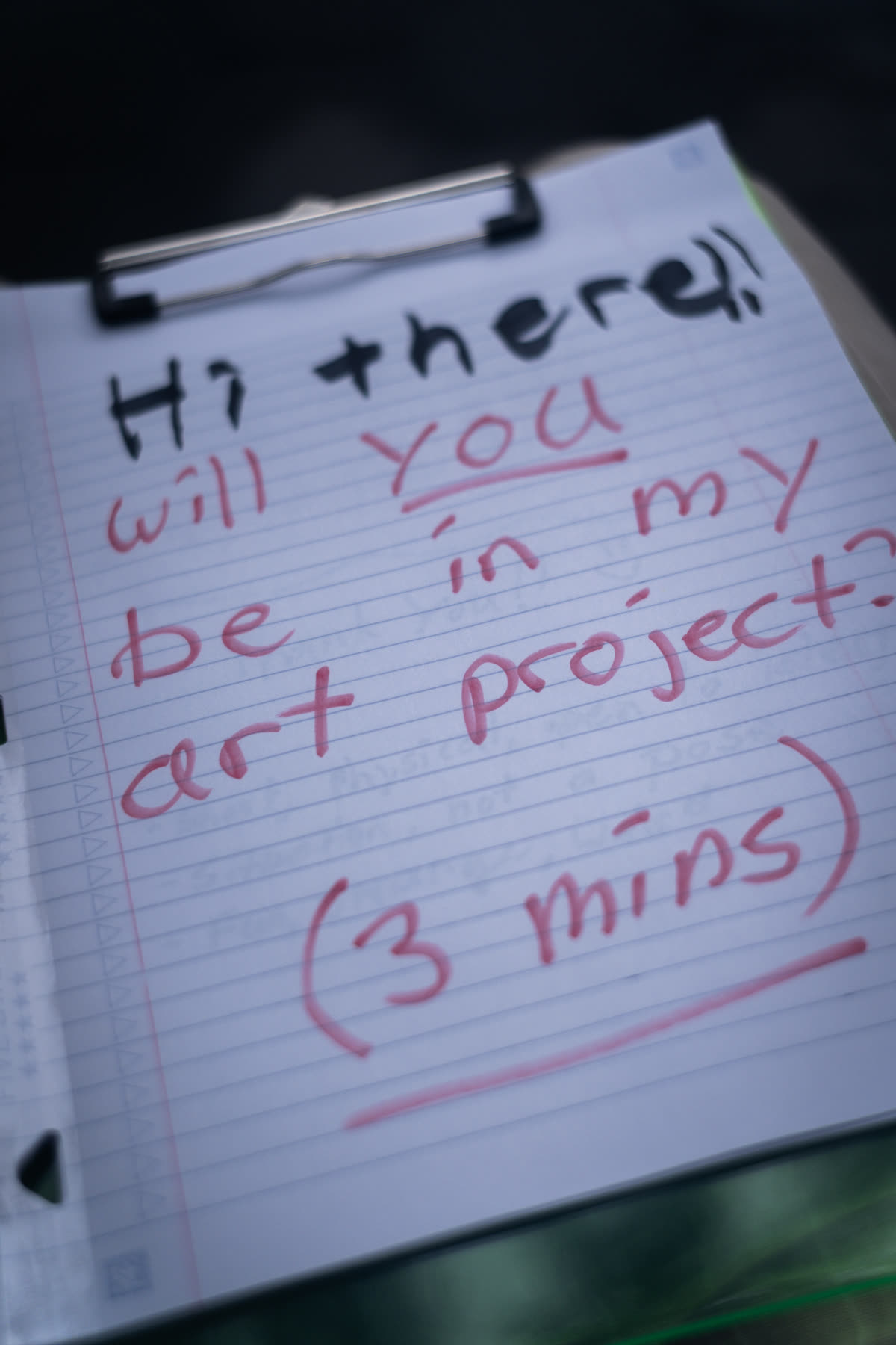 Handwritten clipboard sign asking passersby to join the art project